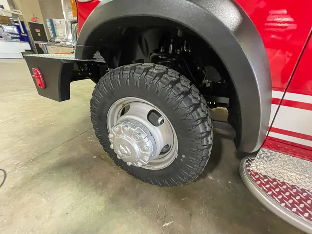 Exterior view of small fire truck showing cab, body compartments, and wheel/tire area.